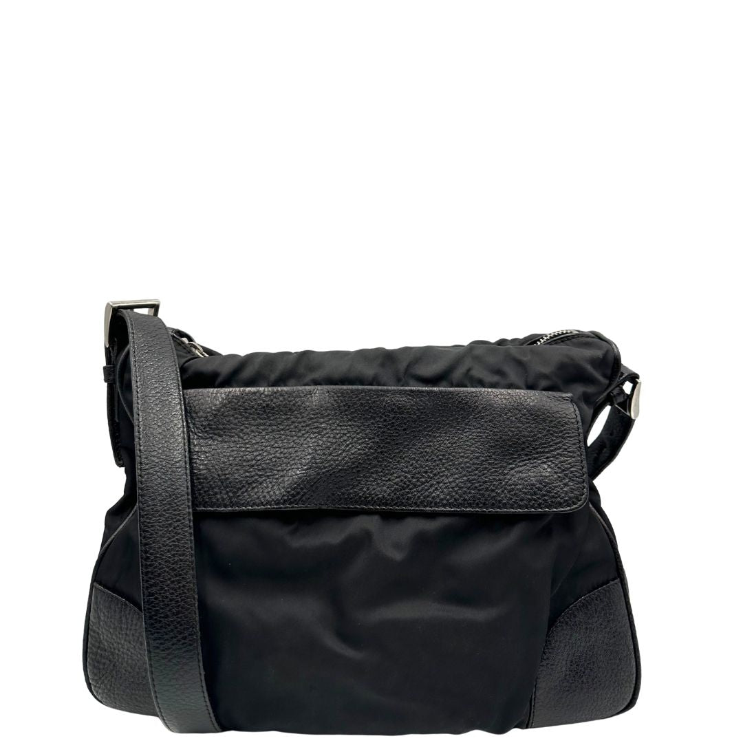 Front di una Borsa Prada in nylon nero con parti metalliche argentate e dettagli in pelle tono su tono. Munita di una tracolla regolabile con fibbie, rifinita con logo triangolare sul lato destro. Originale, usata, di lusso, in condizioni buone.