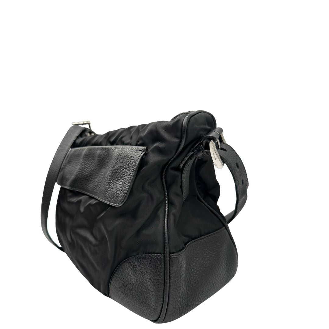 Lato sinistro di una Borsa Prada in nylon nero con parti metalliche argentate e dettagli in pelle tono su tono. Munita di una tracolla regolabile con fibbie, rifinita con logo triangolare sul lato destro. Originale, usata, di lusso, in condizioni buone.