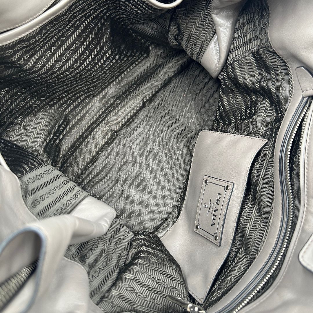 interno Borsa Prada in pelle grigia con parti metalliche argentate; impreziosita da zip laterali e accessorio porta address, munita di doppi manici stondati e una tracolla amovibile e regolabile. Completa di dustbag, di lusso, originale, ottime condizioni.