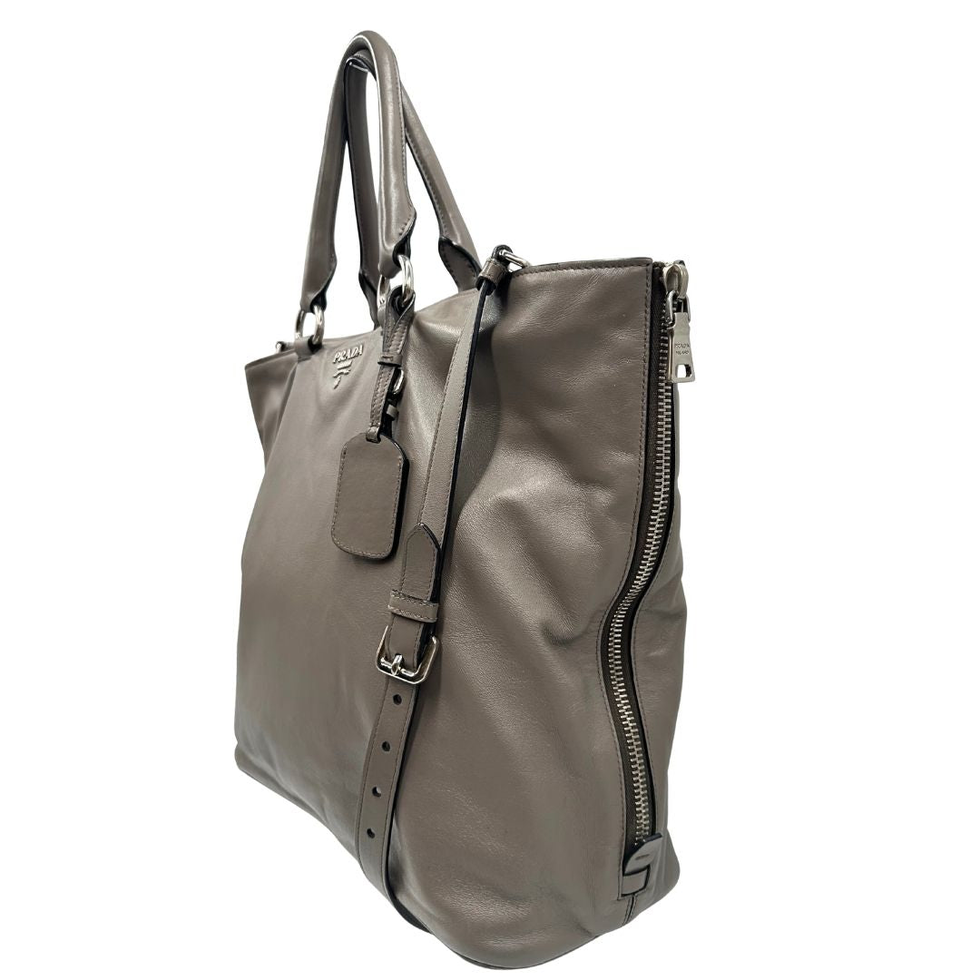 lato Borsa Prada in pelle grigia con parti metalliche argentate; impreziosita da zip laterali e accessorio porta address, munita di doppi manici stondati e una tracolla amovibile e regolabile. Completa di dustbag, di lusso, originale, ottime condizioni. 
