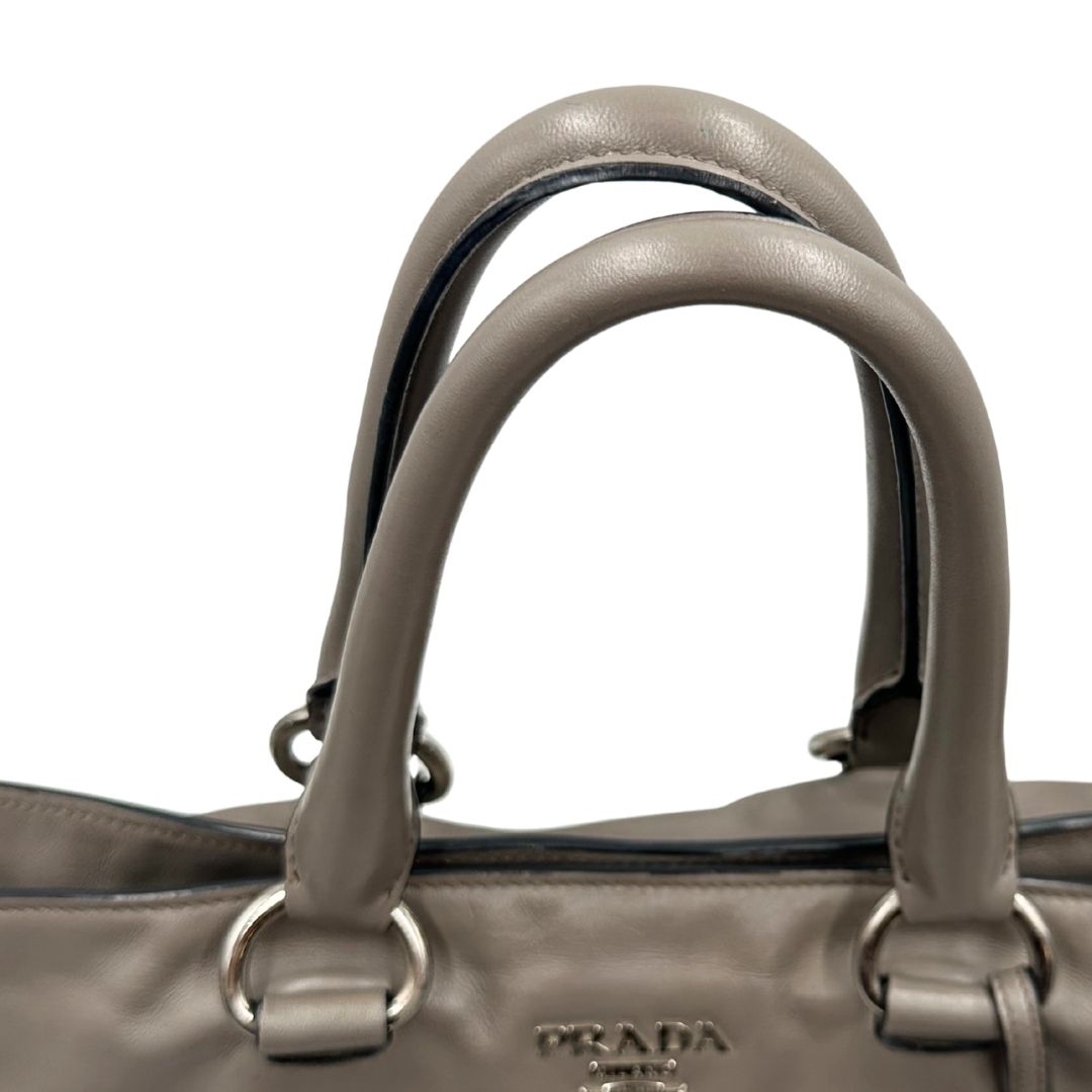 manici Borsa Prada in pelle grigia con parti metalliche argentate; impreziosita da zip laterali e accessorio porta address, munita di doppi manici stondati e una tracolla amovibile e regolabile. Completa di dustbag, di lusso, originale, ottime condizioni.