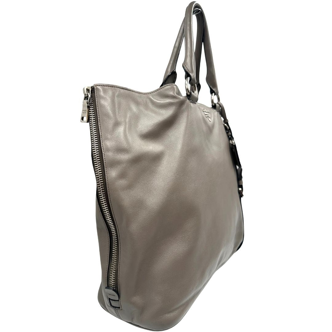lato Borsa Prada in pelle grigia con parti metalliche argentate; impreziosita da zip laterali e accessorio porta address, munita di doppi manici stondati e una tracolla amovibile e regolabile. Completa di dustbag, di lusso, originale, ottime condizioni. 