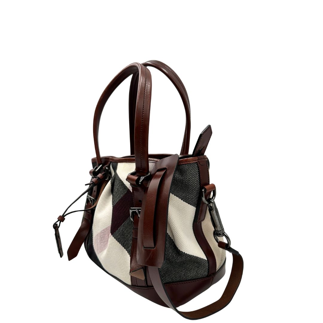 Lato sinistro di una Borsa Tote Burberry in tessuto bianco trama tartan nera e rossa, finiture in pelle marrone e parti metalliche effetto renio, munita di doppie manici e una tracolla regolabile, amovibile con spallaccio. Indossabile a spalla. Originale, usata, di lusso, in ottime condizioni.