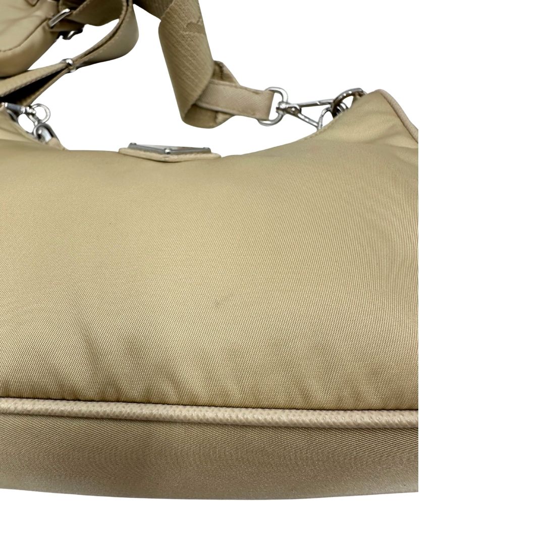 Borsa Prada in Re-Nylon beige con finiture in pelle saffiano tono su tono, munita di un manico in catena e una tracolla in tessuto regolabile e amovibile, impreziosita da pouch rimovibile. Rifinita con parti metalliche argentate e iconico triangolo logato sul front. Indossabile a spalla oppure a tracolla. Originale, usata, di lusso, in ottime condizioni