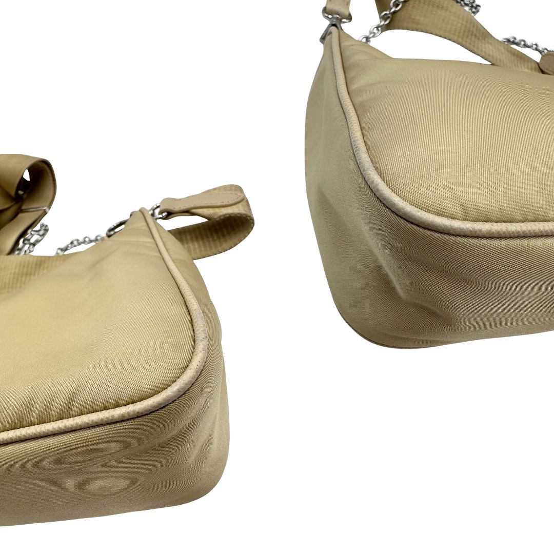 Angoli di una Borsa Prada in Re-Nylon beige con finiture in pelle saffiano tono su tono, munita di un manico in catena e una tracolla in tessuto regolabile e amovibile, impreziosita da pouch rimovibile. Rifinita con parti metalliche argentate e iconico triangolo logato sul front. Indossabile a spalla oppure a tracolla. Originale, usata, di lusso, in ottime condizioni