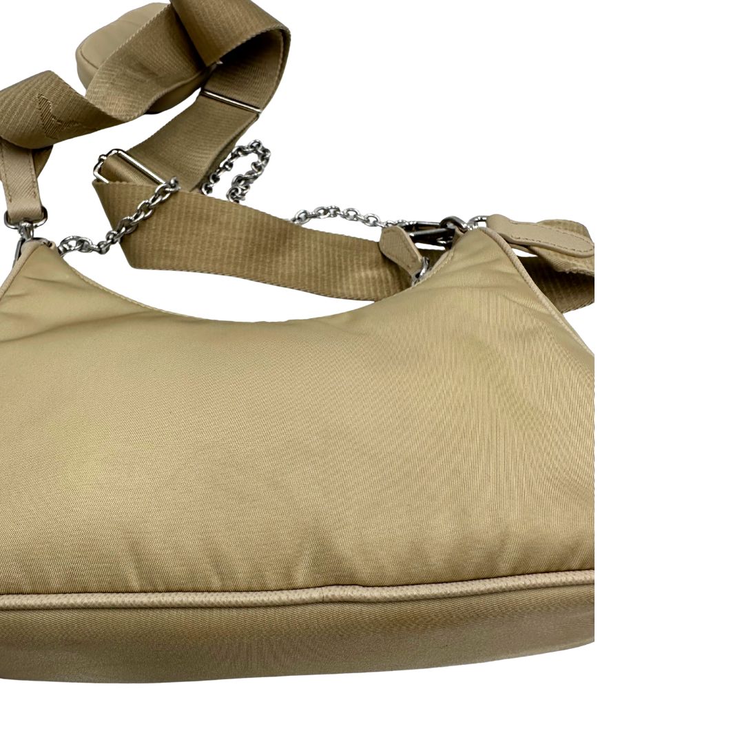 Borsa Prada in Re-Nylon beige con finiture in pelle saffiano tono su tono, munita di un manico in catena e una tracolla in tessuto regolabile e amovibile, impreziosita da pouch rimovibile. Rifinita con parti metalliche argentate e iconico triangolo logato sul front. Indossabile a spalla oppure a tracolla. Originale, usata, di lusso, in ottime condizioni