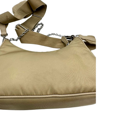 Borsa Prada in Re-Nylon beige con finiture in pelle saffiano tono su tono, munita di un manico in catena e una tracolla in tessuto regolabile e amovibile, impreziosita da pouch rimovibile. Rifinita con parti metalliche argentate e iconico triangolo logato sul front. Indossabile a spalla oppure a tracolla. Originale, usata, di lusso, in ottime condizioni