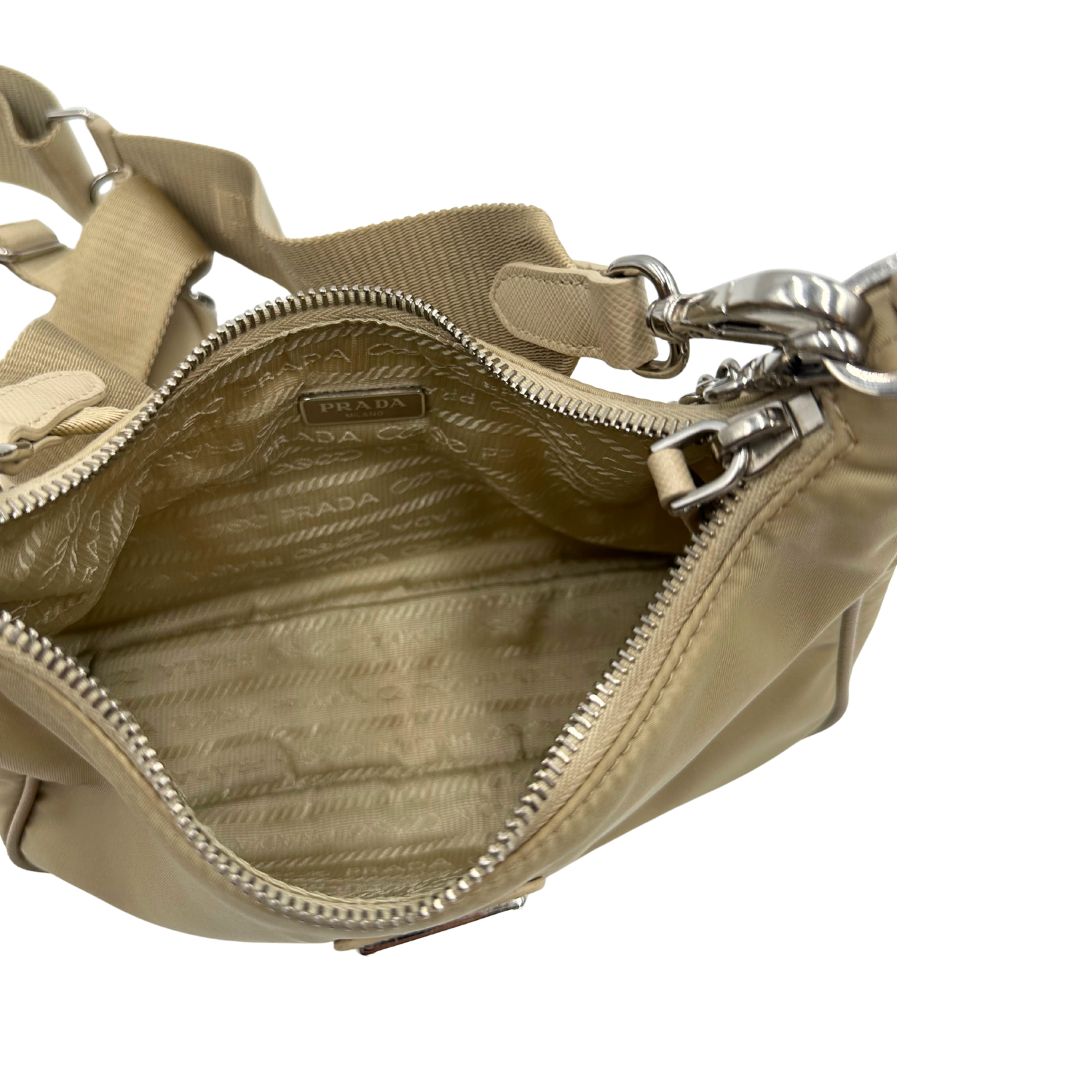 Interno di una Borsa Prada in Re-Nylon beige con finiture in pelle saffiano tono su tono, munita di un manico in catena e una tracolla in tessuto regolabile e amovibile, impreziosita da pouch rimovibile. Rifinita con parti metalliche argentate e iconico triangolo logato sul front. Indossabile a spalla oppure a tracolla. Originale, usata, di lusso, in ottime condizioni