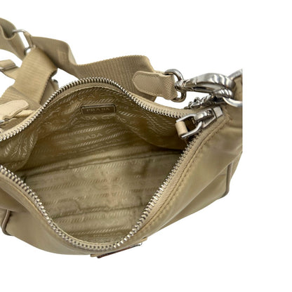 Interno di una Borsa Prada in Re-Nylon beige con finiture in pelle saffiano tono su tono, munita di un manico in catena e una tracolla in tessuto regolabile e amovibile, impreziosita da pouch rimovibile. Rifinita con parti metalliche argentate e iconico triangolo logato sul front. Indossabile a spalla oppure a tracolla. Originale, usata, di lusso, in ottime condizioni