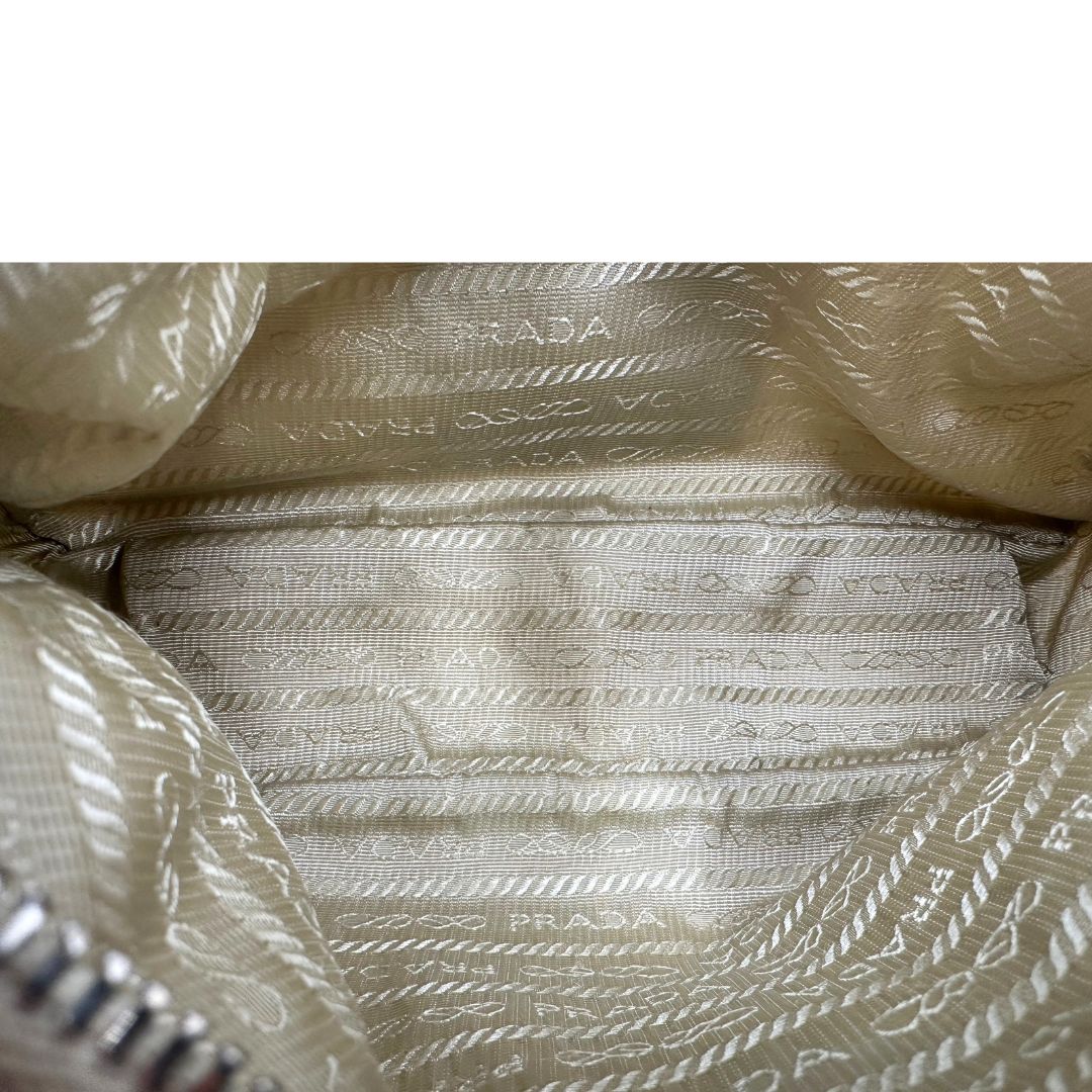 Inerno di una Borsa Prada in Re-Nylon beige con finiture in pelle saffiano tono su tono, munita di un manico in catena e una tracolla in tessuto regolabile e amovibile, impreziosita da pouch rimovibile. Rifinita con parti metalliche argentate e iconico triangolo logato sul front. Indossabile a spalla oppure a tracolla. Originale, usata, di lusso, in ottime condizioni
