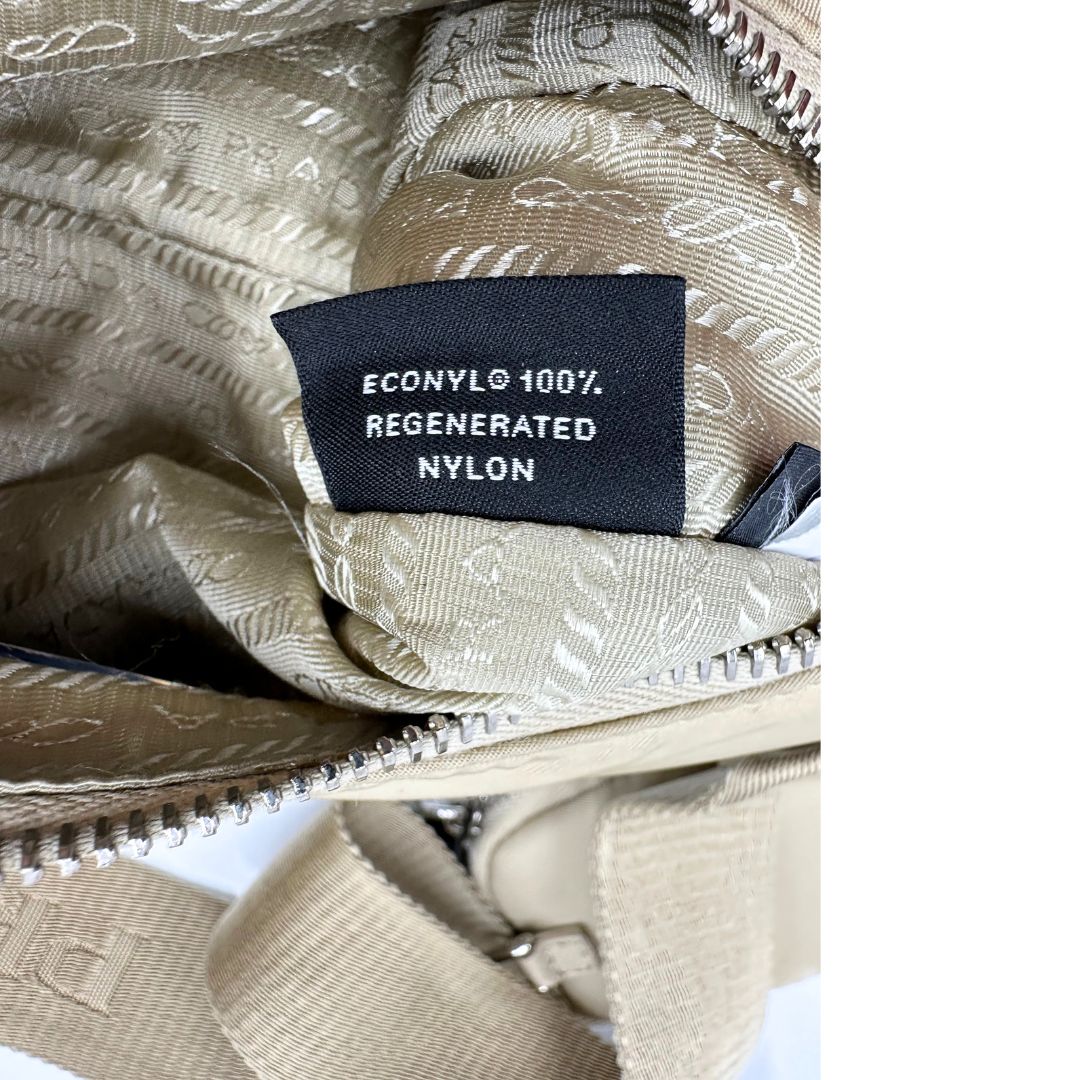 Borsa Prada in Re-Nylon beige con finiture in pelle saffiano tono su tono, munita di un manico in catena e una tracolla in tessuto regolabile e amovibile, impreziosita da pouch rimovibile. Rifinita con parti metalliche argentate e iconico triangolo logato sul front. Indossabile a spalla oppure a tracolla. Originale, usata, di lusso, in ottime condizioni