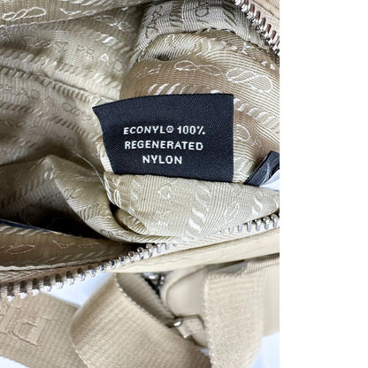 Borsa Prada in Re-Nylon beige con finiture in pelle saffiano tono su tono, munita di un manico in catena e una tracolla in tessuto regolabile e amovibile, impreziosita da pouch rimovibile. Rifinita con parti metalliche argentate e iconico triangolo logato sul front. Indossabile a spalla oppure a tracolla. Originale, usata, di lusso, in ottime condizioni