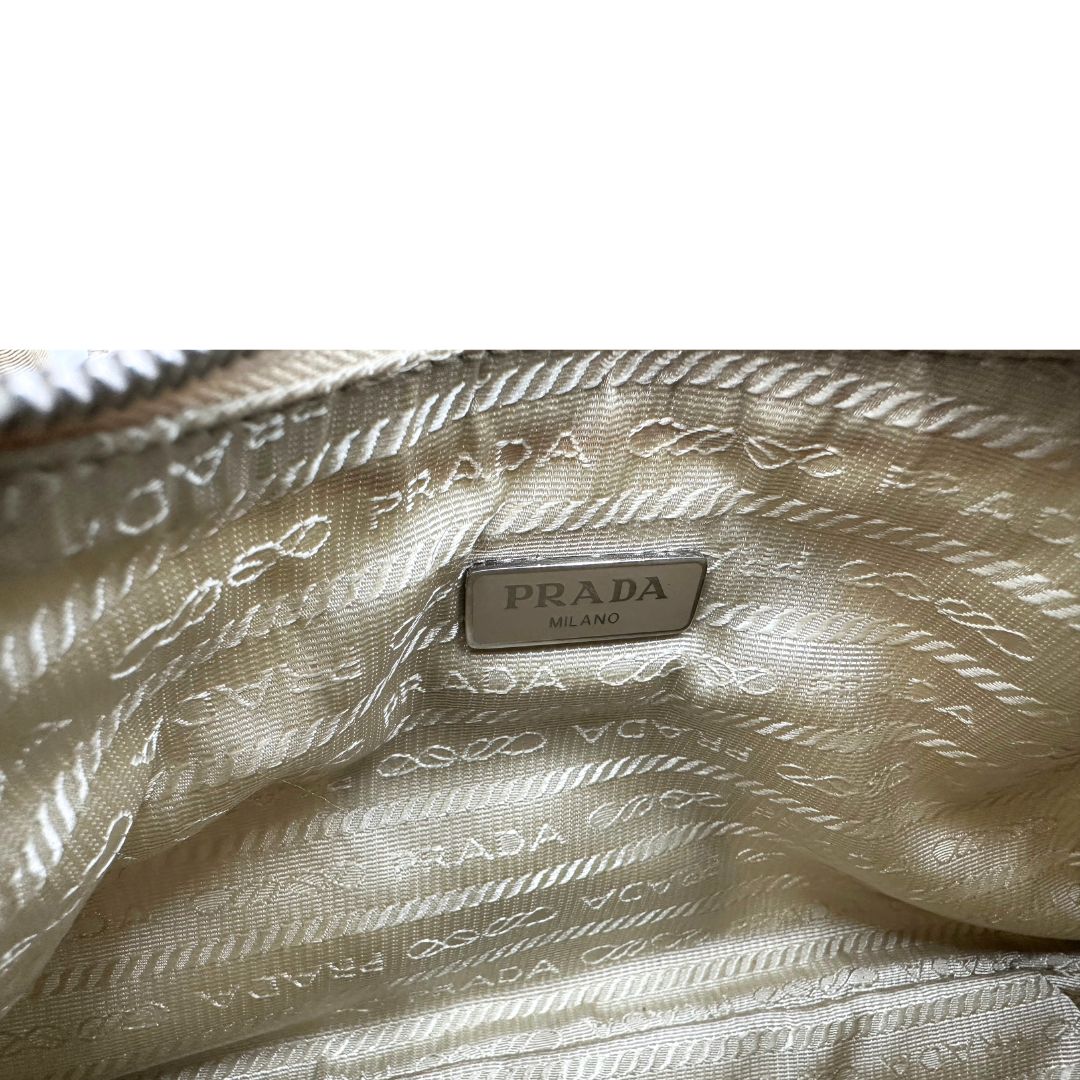 Interno di una Borsa Prada in Re-Nylon beige con finiture in pelle saffiano tono su tono, munita di un manico in catena e una tracolla in tessuto regolabile e amovibile, impreziosita da pouch rimovibile. Rifinita con parti metalliche argentate e iconico triangolo logato sul front. Indossabile a spalla oppure a tracolla. Originale, usata, di lusso, in ottime condizioni