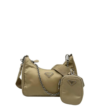 Front di una Borsa Prada in Re-Nylon beige con finiture in pelle saffiano tono su tono, munita di un manico in catena e una tracolla in tessuto regolabile e amovibile, impreziosita da pouch rimovibile. Rifinita con parti metalliche argentate e iconico triangolo logato sul front. Indossabile a spalla oppure a tracolla. Originale, usata, di lusso, in ottime condizioni