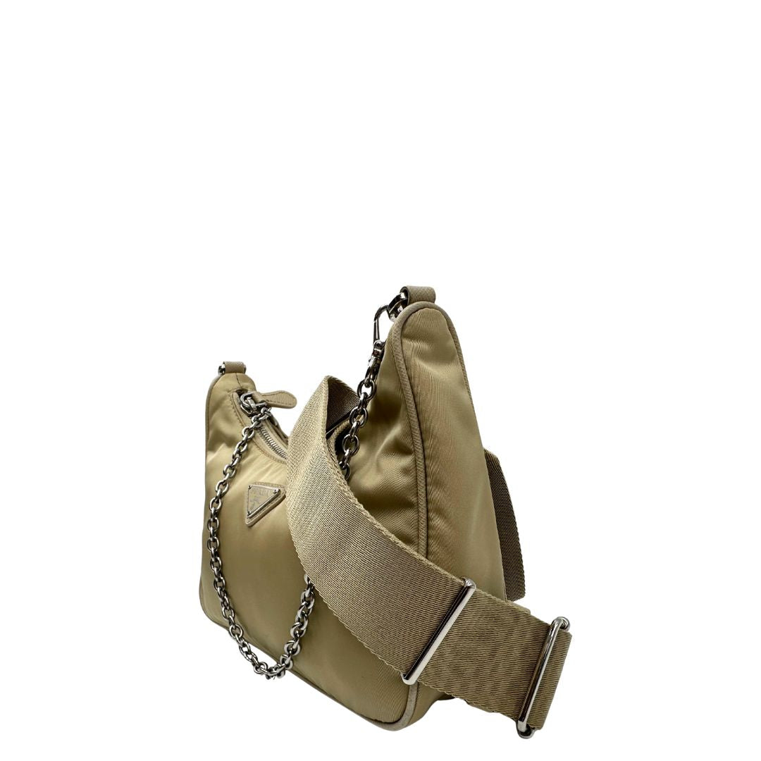 Lato sinistro di una Borsa Prada in Re-Nylon beige con finiture in pelle saffiano tono su tono, munita di un manico in catena e una tracolla in tessuto regolabile e amovibile, impreziosita da pouch rimovibile. Rifinita con parti metalliche argentate e iconico triangolo logato sul front. Indossabile a spalla oppure a tracolla. Originale, usata, di lusso, in ottime condizioni