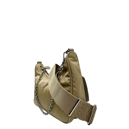 Lato sinistro di una Borsa Prada in Re-Nylon beige con finiture in pelle saffiano tono su tono, munita di un manico in catena e una tracolla in tessuto regolabile e amovibile, impreziosita da pouch rimovibile. Rifinita con parti metalliche argentate e iconico triangolo logato sul front. Indossabile a spalla oppure a tracolla. Originale, usata, di lusso, in ottime condizioni