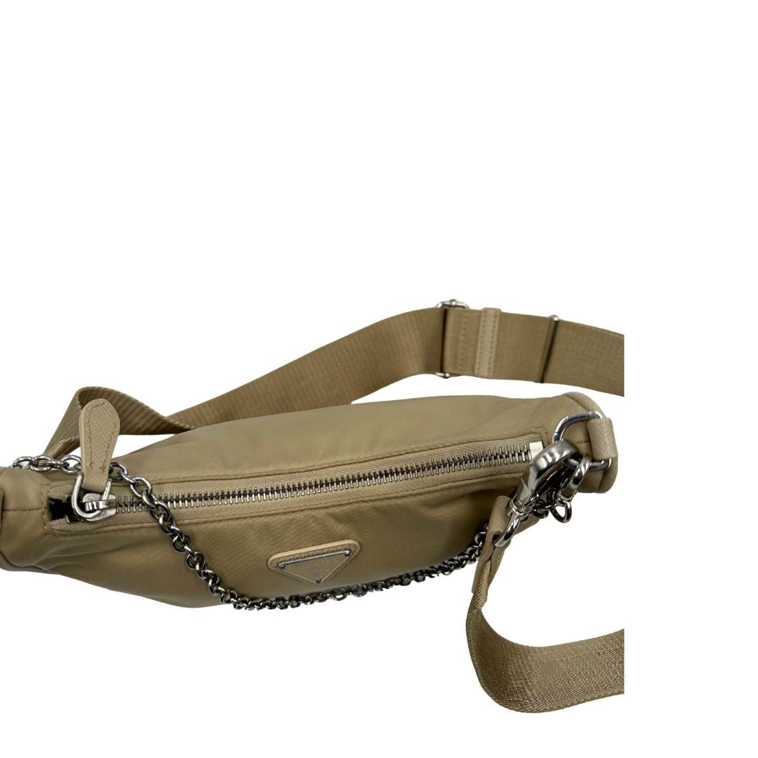 Chiusura di una Borsa Prada in Re-Nylon beige con finiture in pelle saffiano tono su tono, munita di un manico in catena e una tracolla in tessuto regolabile e amovibile, impreziosita da pouch rimovibile. Rifinita con parti metalliche argentate e iconico triangolo logato sul front. Indossabile a spalla oppure a tracolla. Originale, usata, di lusso, in ottime condizioni.