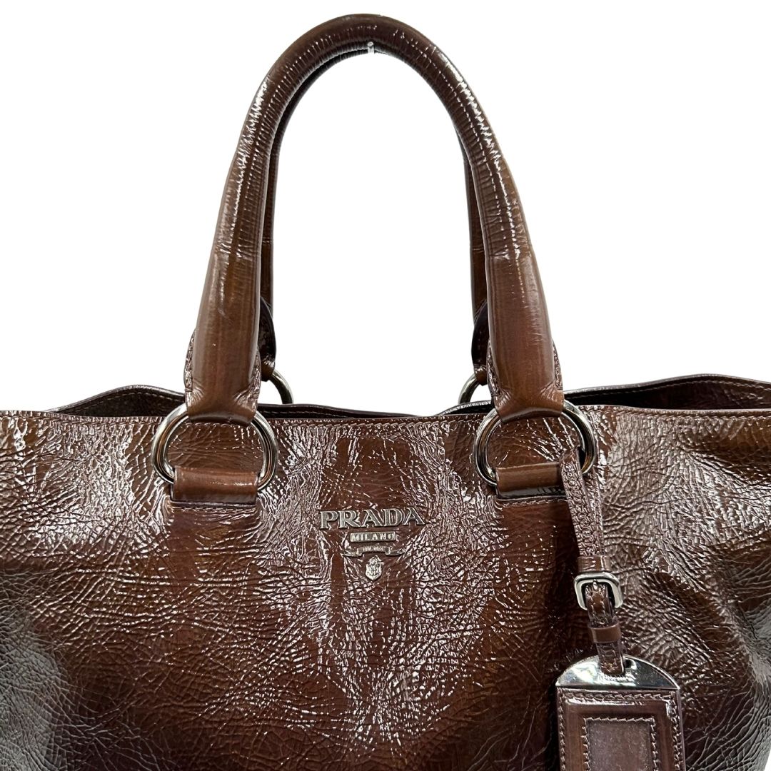 manici Borsa Prada in pelle lucida color cioccolato con parti metalliche argentate; munita di un accessorio porta address e doppi manici. Completa di dustbag, di lusso, originale, ottime condizioni. 
