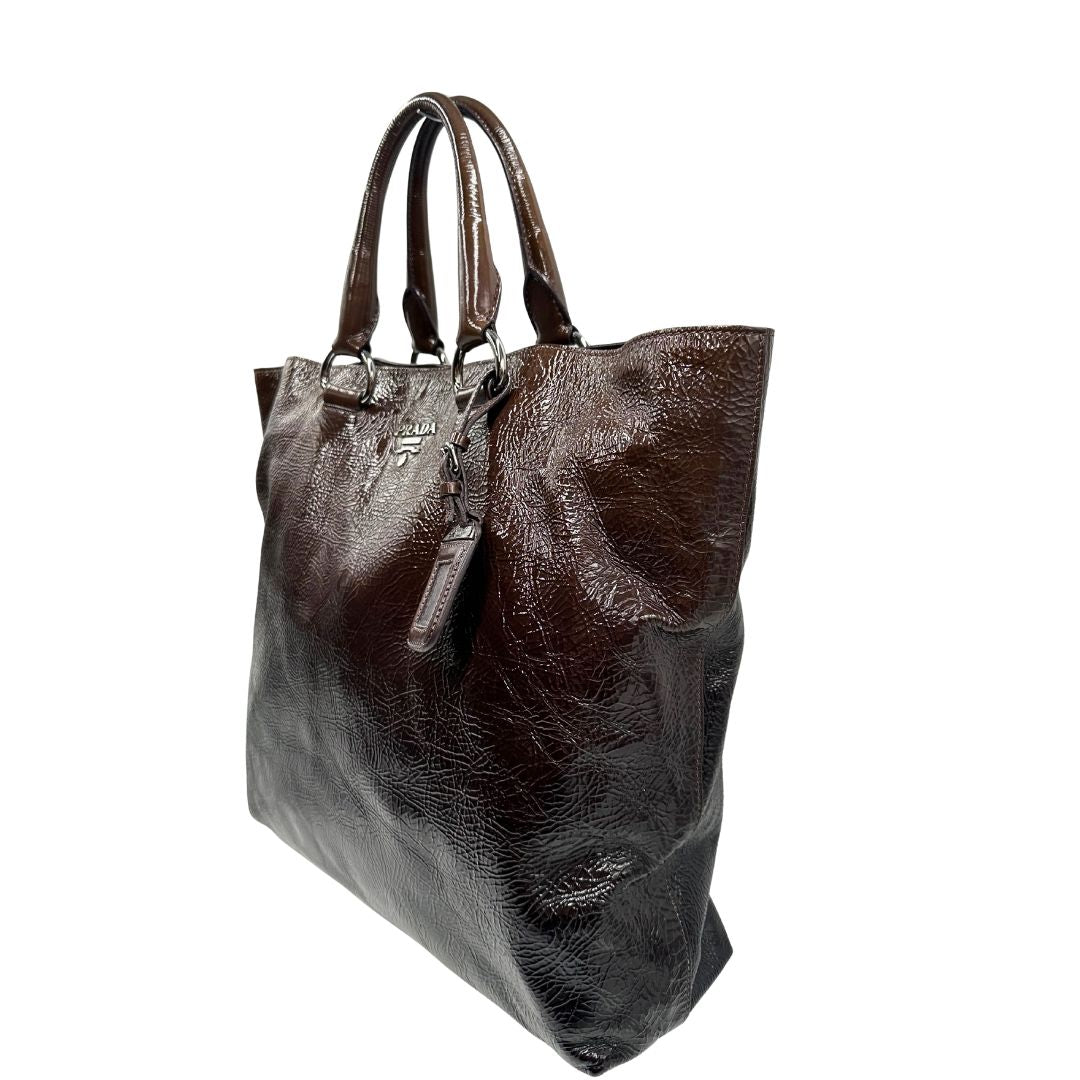 lato Borsa Prada in pelle lucida color cioccolato con parti metalliche argentate; munita di un accessorio porta address e doppi manici. Completa di dustbag, di lusso, originale, ottime condizioni. 