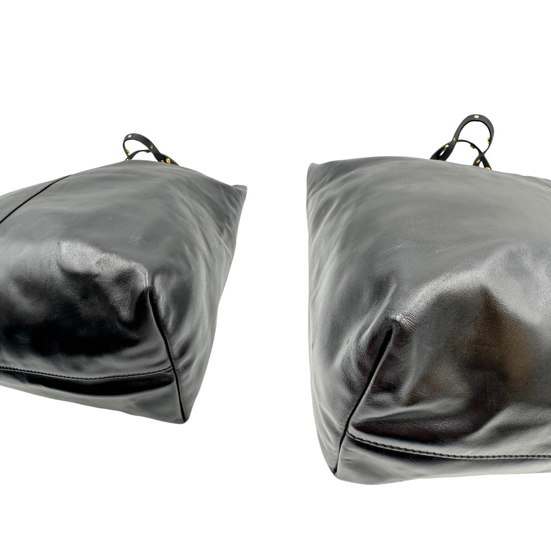 Angoli di una Shopper Versace in pelle nera con parti metalliche dorate munita di due manici con borchie dorate decorative. Indossabile a spalla. N.B. Pochette mancante e punto di aggancio in pelle tagliato dalla precedente cliente. Originale, usata, di lusso, in ottime condizioni.