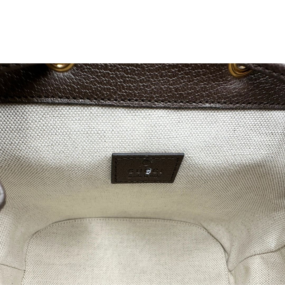 Interno di uno zaino Gucci in canvas beige GG con finiture in pelle marroni e parti metalliche dorate. Iconica striscia Web in verde/rosso sulla patta, impreziosita da un manico in catena amovibile e cinghie in pelle regolabili. Completo di dustbag.