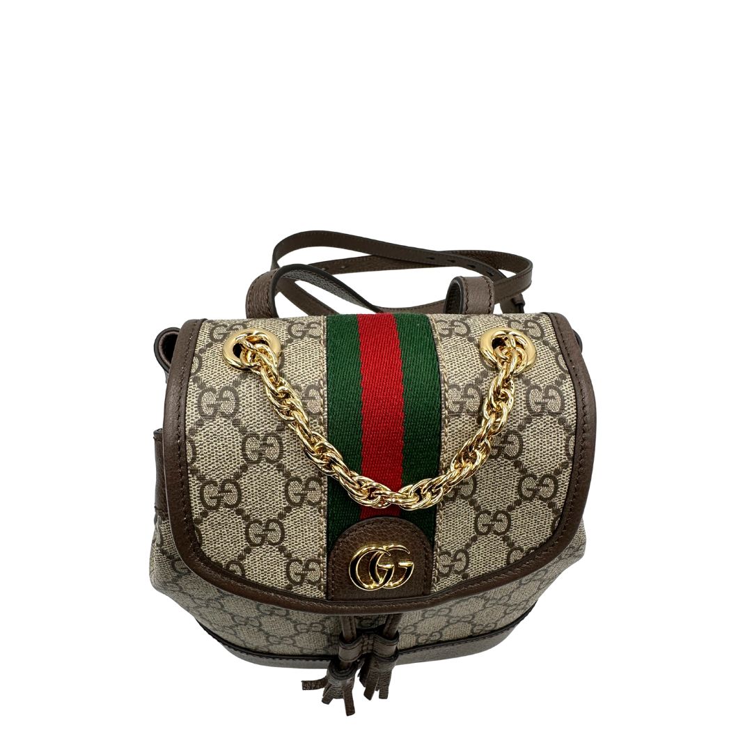 Vista superiore di uno zaino Gucci in canvas beige GG con finiture in pelle marroni e parti metalliche dorate. Iconica striscia Web in verde/rosso sulla patta, impreziosita da un manico in catena amovibile e cinghie in pelle regolabili. Completo di dustbag.