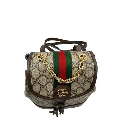Vista superiore di uno zaino Gucci in canvas beige GG con finiture in pelle marroni e parti metalliche dorate. Iconica striscia Web in verde/rosso sulla patta, impreziosita da un manico in catena amovibile e cinghie in pelle regolabili. Completo di dustbag.