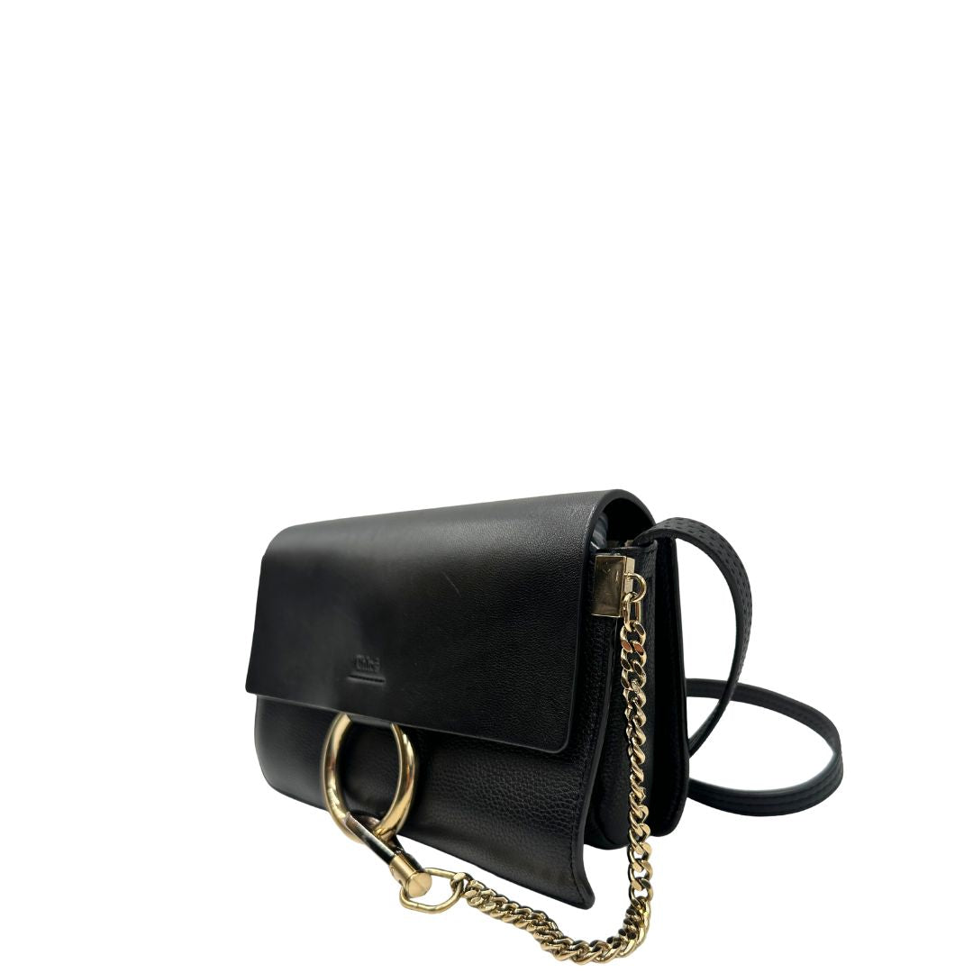 Lato sinistro di una Borsa Chloé Faye in pelle martellata nera con parti metalliche dorate, munita di una tracolla regolabile. Impreziosita di una chiusura principale con gancio con l'iconico anello sul davanti, collegato a una piccola catena a moschettone. Indossabile a tracolla .Originale, usata, di lusso, in ottime condizioni.