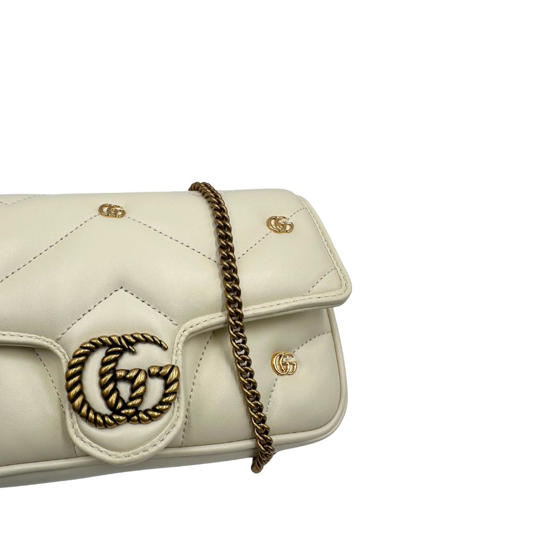Borsa Gucci GG Marmont in pelle matelassé color bianco latte, caratterizzata dalla classica trapuntatura a chevron e dagli iconici dettagli GG in metallo dorato anticato. Dotata di tracolla a catena amovibile. Presente un pouch portamonete con zip rimovibile. Completa di dustbag. Originale, usata, di lusso,in condizioni eccellenti.