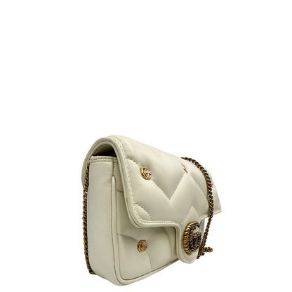 Lato destro di una Borsa Gucci GG Marmont in pelle matelassé color bianco latte, caratterizzata dalla classica trapuntatura a chevron e dagli iconici dettagli GG in metallo dorato anticato. Dotata di tracolla a catena amovibile. Presente un pouch portamonete con zip rimovibile. Completa di dustbag. Originale, usata, di lusso, in condizioni eccellenti.