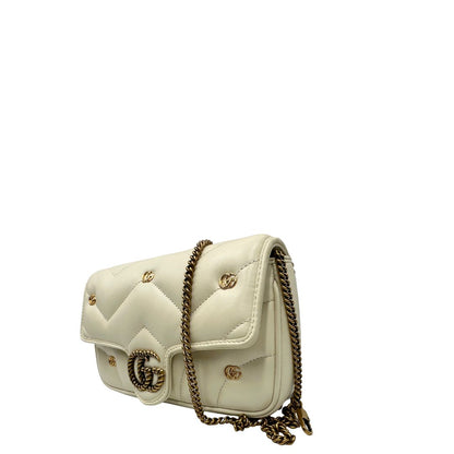 Lato sinistro di una Borsa Gucci GG Marmont in pelle matelassé color bianco latte, caratterizzata dalla classica trapuntatura a chevron e dagli iconici dettagli GG in metallo dorato anticato. Dotata di tracolla a catena amovibile. Presente un pouch portamonete con zip rimovibile. Completa di dustbag. Originale, usata, di lusso in condizioni eccellenti.
