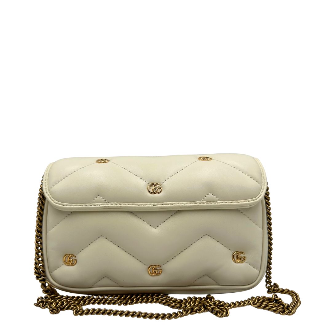 Retro di una Borsa Gucci GG Marmont in pelle matelassé color bianco latte, caratterizzata dalla classica trapuntatura a chevron e dagli iconici dettagli GG in metallo dorato anticato. Dotata di tracolla a catena amovibile. Presente un pouch portamonete con zip rimovibile. Completa di dustbag. Originale, usata, di lusso, in condizioni eccellenti.