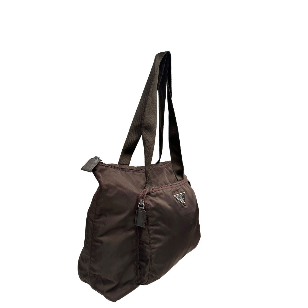 lato Borsa Prada in nylon marrone scuro con parti metalliche argentate , munita di doppi manici in tessuto, indossabile a spalla. 