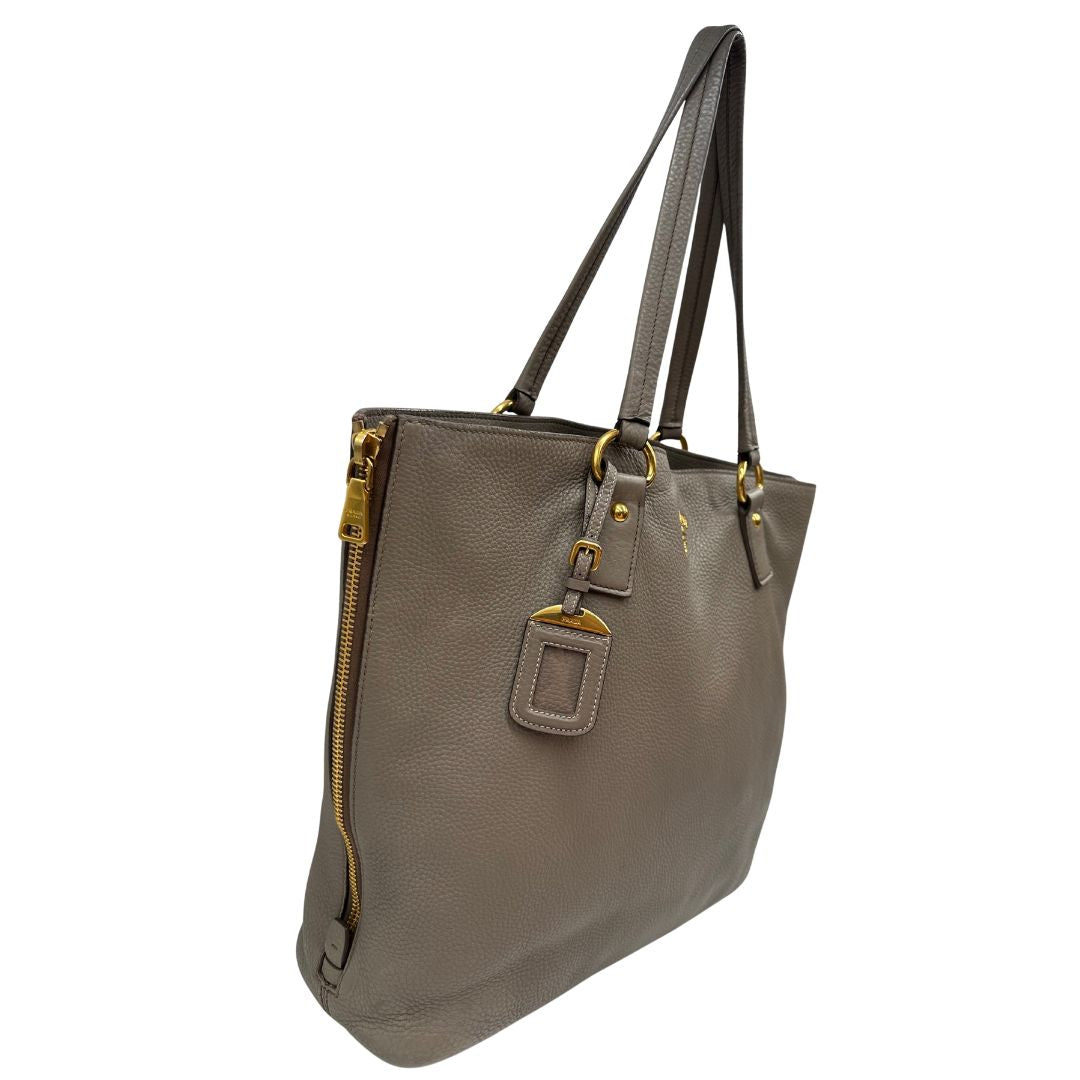 lato Borsa Prada in pelle grigia martellata con parti metalliche dorate; munita di cerniere laterali e doppi manici, indossabile a spalla, di lusso, originale, ottime condizioni, usata. 