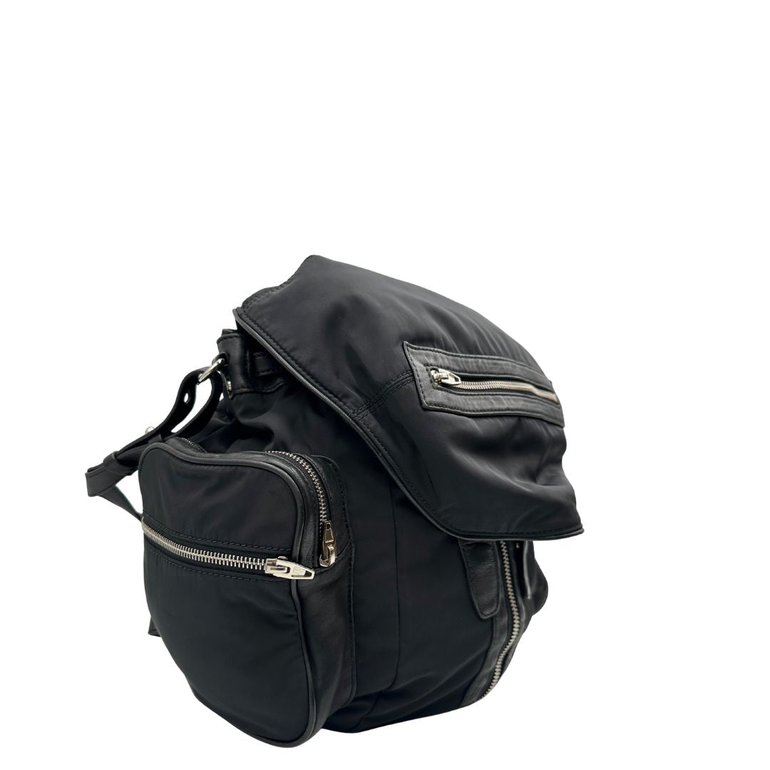 Laterale sinistro di uno zaino Alexander Wang in nylon nero e finiture in pelle tono su tono. Parti metalliche argentate; munito di doppie bretelle e una tracolla. Indossabile come zaino o a tracolla.
