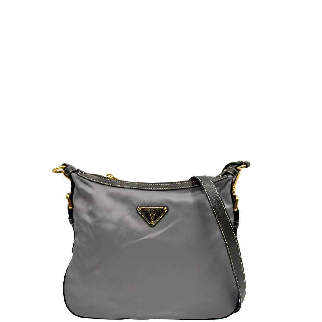 Front di una Borsa Prada in nylon Grigia con finiture in pelle nera e parti metalliche dorate; munita di una tracolla in tessuto regolabile e tag porta address. Originale, usata, di lusso in ottime condizioni.