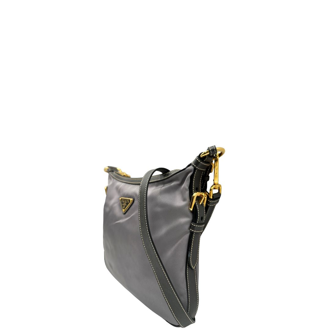 Lato sinistro di una Borsa Prada in nylon Grigia con finiture in pelle nera e parti metalliche dorate; munita di una tracolla in tessuto regolabile e tag porta address. Originale, usata, di lusso in ottime condizioni.