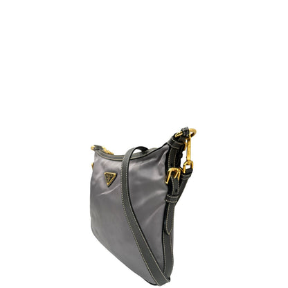 Lato sinistro di una Borsa Prada in nylon Grigia con finiture in pelle nera e parti metalliche dorate; munita di una tracolla in tessuto regolabile e tag porta address. Originale, usata, di lusso in ottime condizioni.