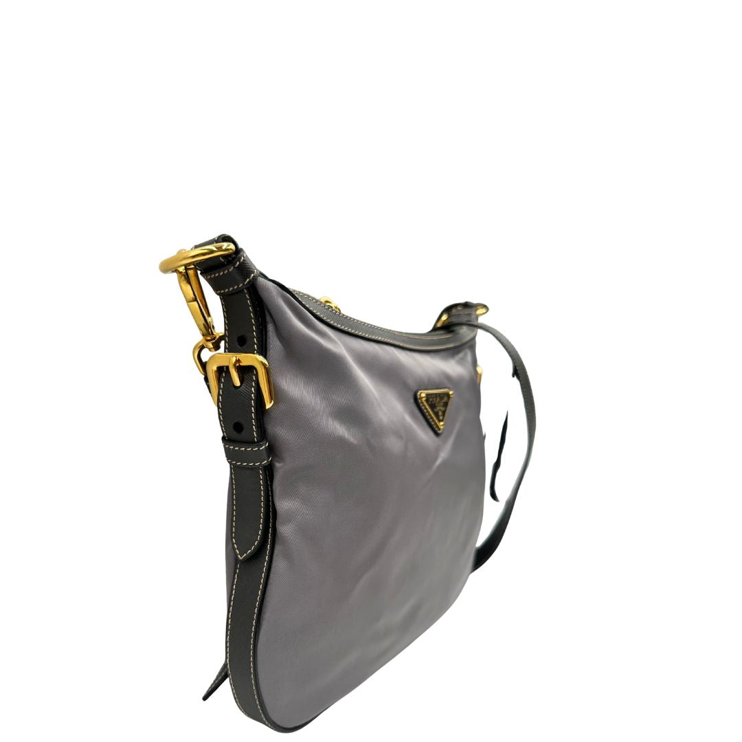 Lato destro di una Borsa Prada in nylon Grigia con finiture in pelle nera e parti metalliche dorate; munita di una tracolla in tessuto regolabile e tag porta address. Originale, usata, di lusso in ottime condizioni.