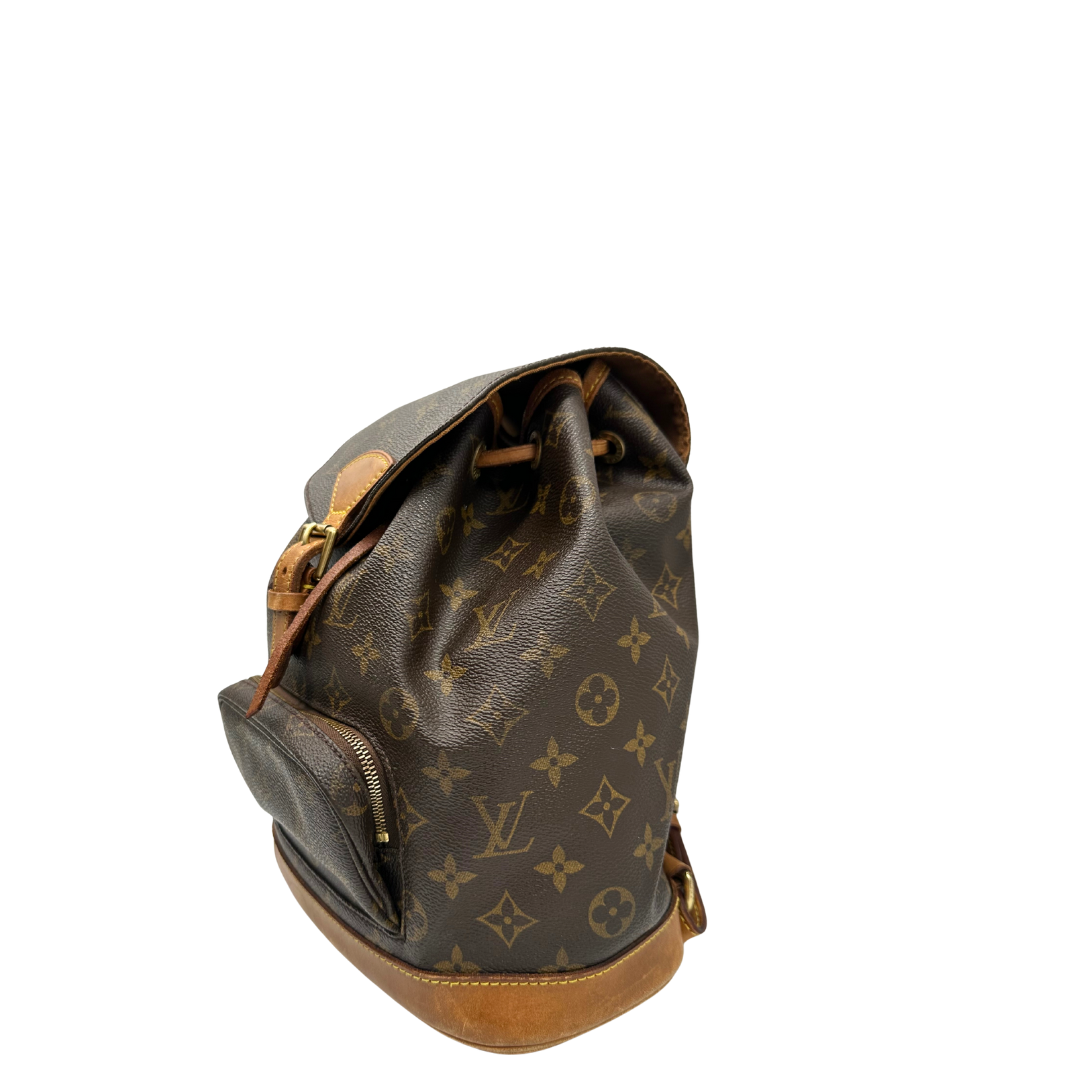 Lato sinistro di un Zaino Montsouris PM in canvas marrone monogram con finiture in vacchetta naturale e parti metalliche dorate, munito di un Anello da portare a mano e una tracolle in vacchetta regolabile con fibbie. Originale, usato , di lusso, in ottime condizioni.