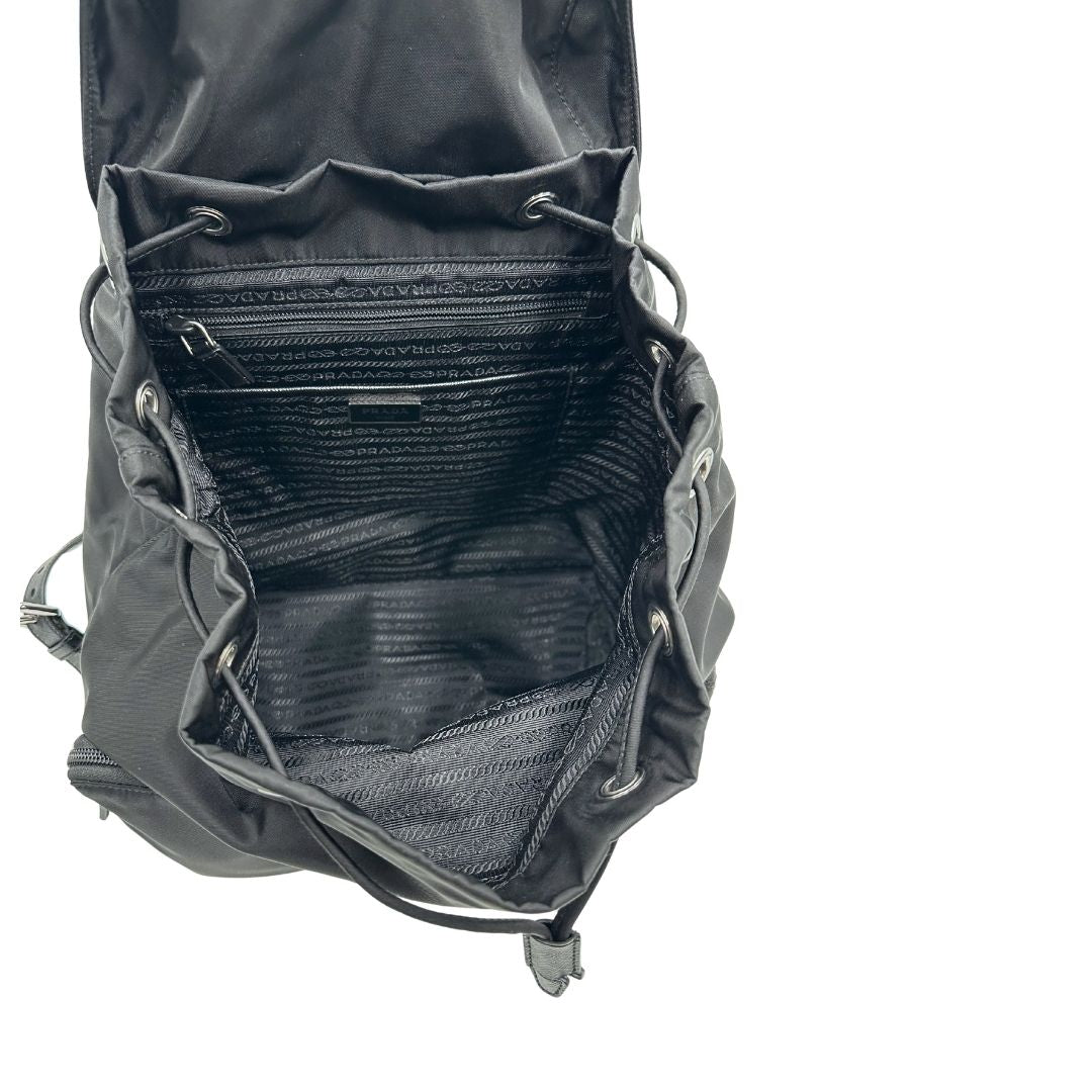 Interno di un Zaino Prada in tessuto nylon nero e finiture in pelle saffiano tono su tono. Parti metalliche argentate; munito di doppie bretelle in tessuto regolabili. Completo di corredo e card d'autenticità. Originale, usato, di lusso, in condizioni eccellenti.