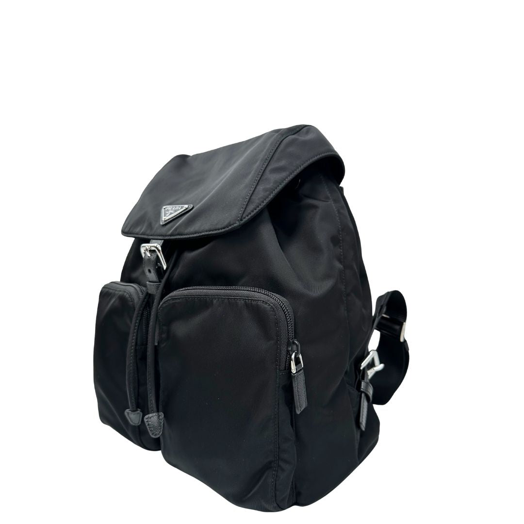 Lato sinistro di una Zaino Prada in tessuto nylon nero e finiture in pelle saffiano tono su tono. Parti metalliche argentate; munito di doppie bretelle in tessuto regolabili. Completo di corredo e card d'autenticità. Originale, usato, di lusso, in condizioni eccellenti.