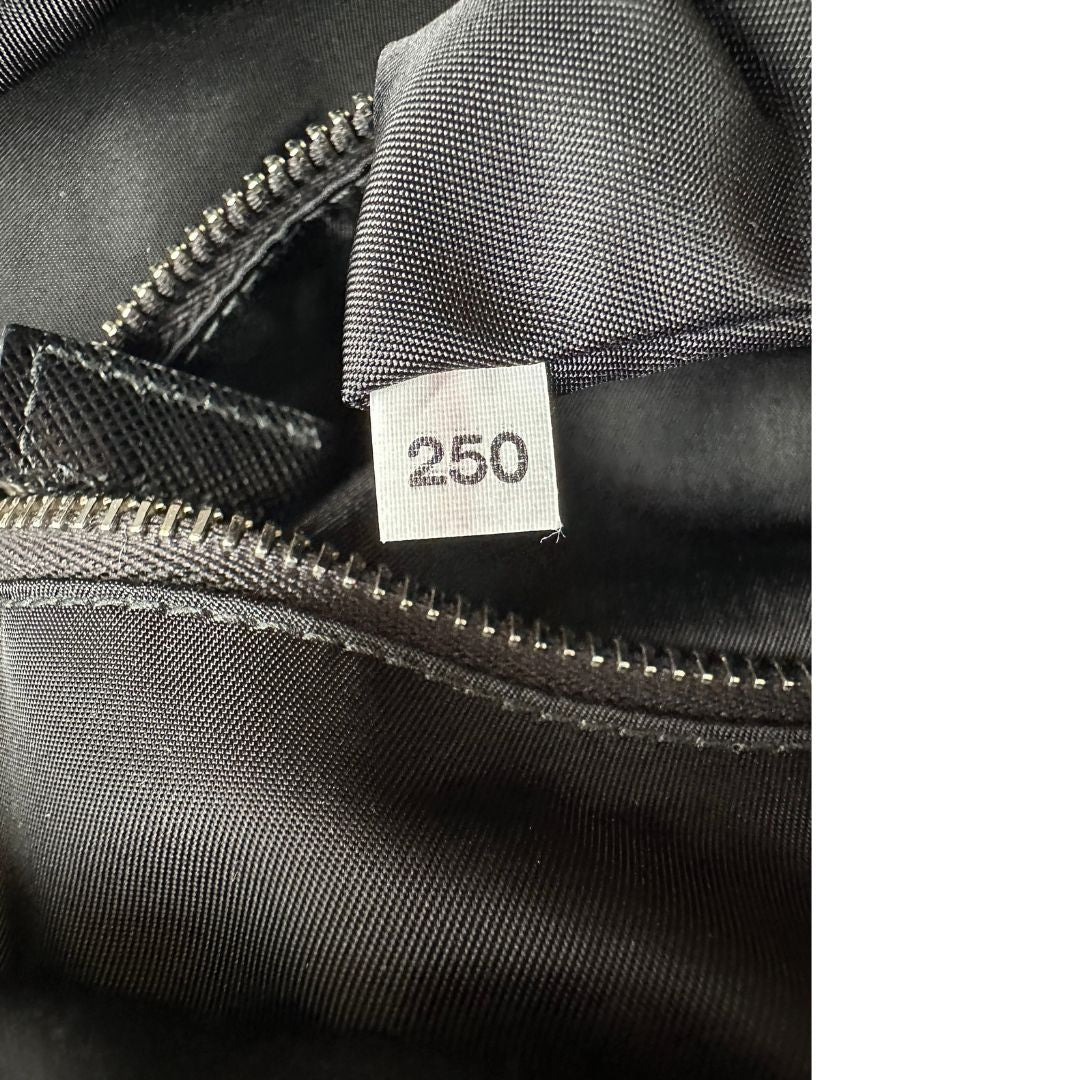 Codice di uno zaino Prada x Adidas in Re-Nylon con chiusura a zip. Struttura con tasca frontale a zip e tasca superiore integrata negli spallacci. Spallacci regolabili con imbottitura e pannello posteriore in mesh. Dettagli con logo triangolo Prada sul lato superiore e branding Prada Re-Nylon e Adidas sul fianco.