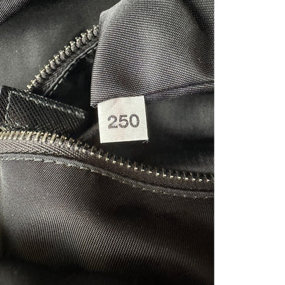 Codice di uno zaino Prada x Adidas in Re-Nylon con chiusura a zip. Struttura con tasca frontale a zip e tasca superiore integrata negli spallacci. Spallacci regolabili con imbottitura e pannello posteriore in mesh. Dettagli con logo triangolo Prada sul lato superiore e branding Prada Re-Nylon e Adidas sul fianco.