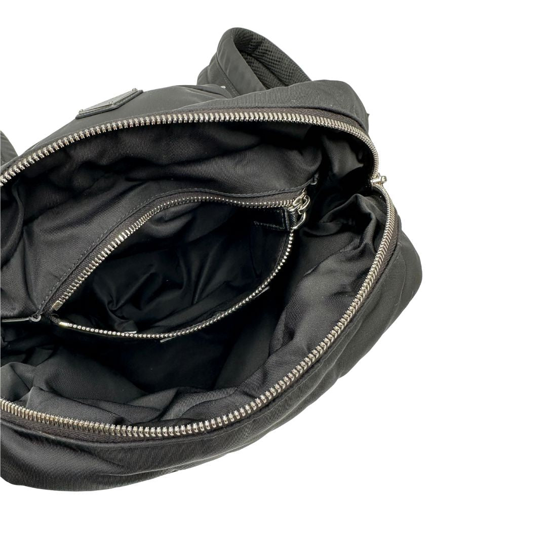 Interno di uno zaino Prada x Adidas in Re-Nylon con chiusura a zip. Struttura con tasca frontale a zip e tasca superiore integrata negli spallacci. Spallacci regolabili con imbottitura e pannello posteriore in mesh. Dettagli con logo triangolo Prada sul lato superiore e branding Prada Re-Nylon e Adidas sul fianco.