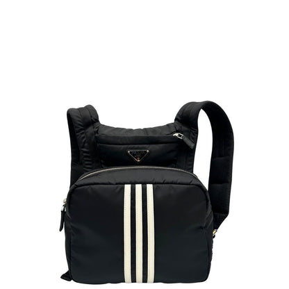 Front di uno zaino Prada x Adidas in Re-Nylon con chiusura a zip. Struttura con tasca frontale a zip e tasca superiore integrata negli spallacci. Spallacci regolabili con imbottitura e pannello posteriore in mesh. Dettagli con logo triangolo Prada sul lato superiore e branding Prada Re-Nylon e Adidas sul fianco.