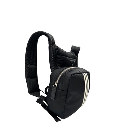 Laterale sinistro di uno zaino Prada x Adidas in Re-Nylon con chiusura a zip. Struttura con tasca frontale a zip e tasca superiore integrata negli spallacci. Spallacci regolabili con imbottitura e pannello posteriore in mesh. Dettagli con logo triangolo Prada sul lato superiore e branding Prada Re-Nylon e Adidas sul fianco.