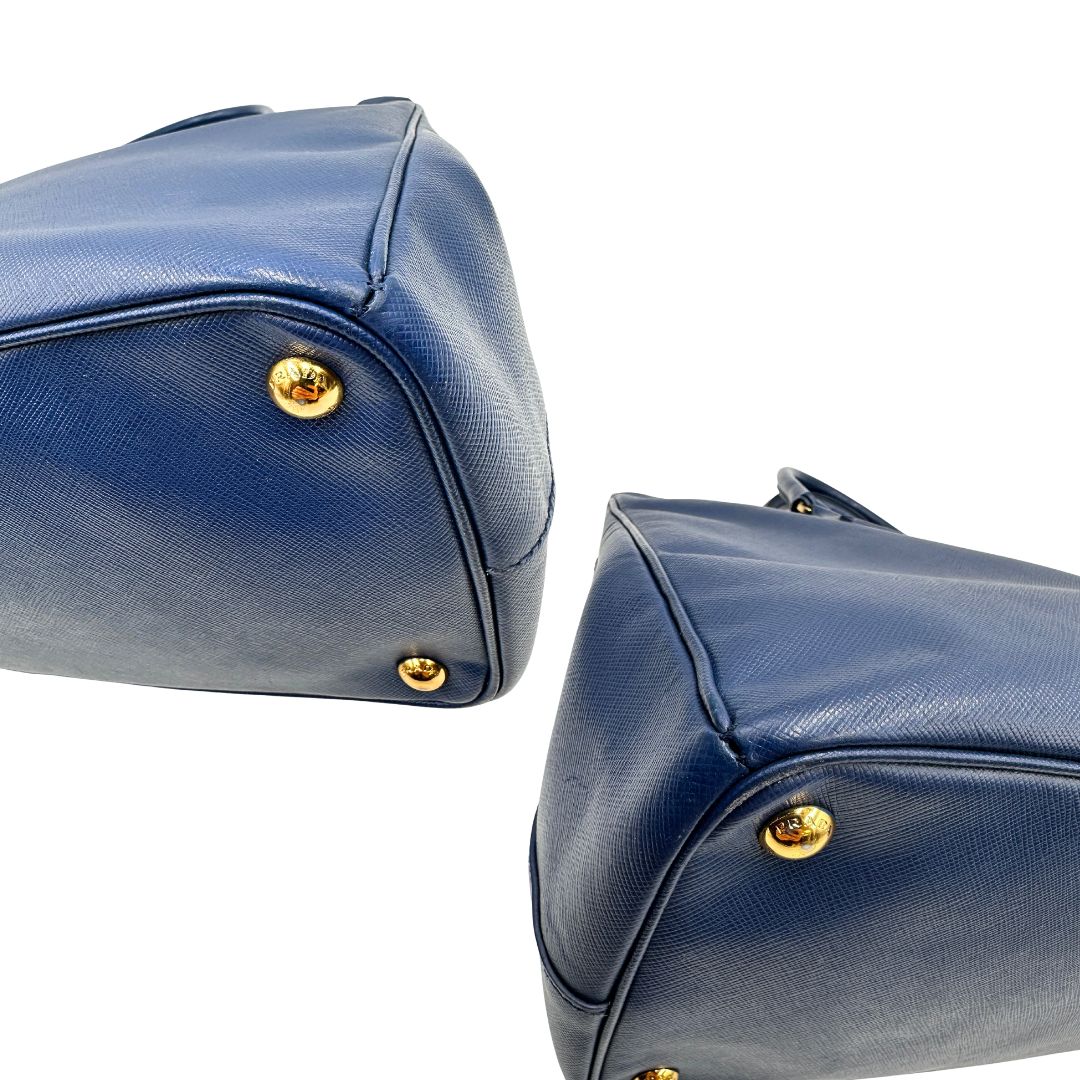 angoli Borsa Prada in pelle saffiano blu con parti metalliche dorate; munita di doppi manici stondati e impreziosita da una clochette portachiavi, di lusso, originale, ottime condizioni. 