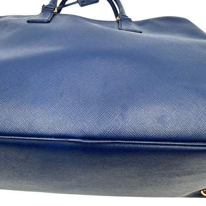 base Borsa Prada in pelle saffiano blu con parti metalliche dorate; munita di doppi manici stondati e impreziosita da una clochette portachiavi, di lusso, originale, ottime condizioni. 