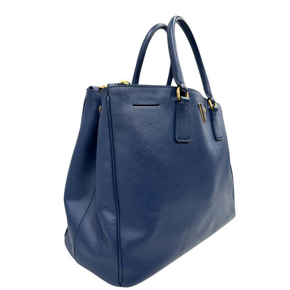 lato Borsa Prada in pelle saffiano blu con parti metalliche dorate; munita di doppi manici stondati e impreziosita da una clochette portachiavi, di lusso, originale, ottime condizioni. 